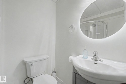Contemporary bathroom vanity with integrated sink, chrome faucet, and backlit oval mirror - 710 Glenwright Court, Edmonton, AB 