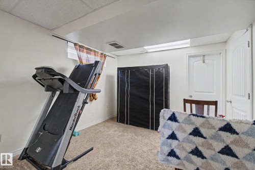 Carpeted room featuring a drop ceiling, white painted walls, and an arched panel interior door - 710 Glenwright Court, Edmonton, AB 