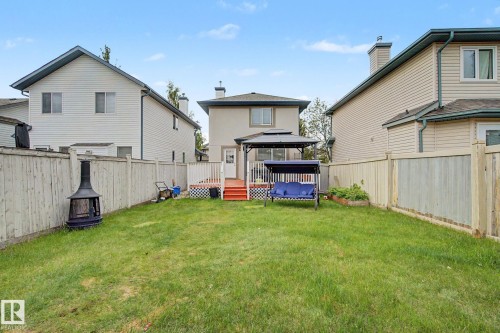 Expansive backyard with a manicured lawn, full wood fencing, and a multi-level deck featuring white railings and red-painted stairs - 710 Glenwright Court, Edmonton, AB 