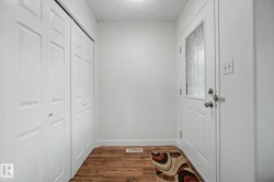 Entryway with wood-finish flooring, a white paneled door with frosted glass insert, and bi-fold closet doors - 