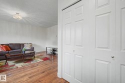 Living area with wood-finish flooring, white walls, and a contemporary ceiling light fixture - 