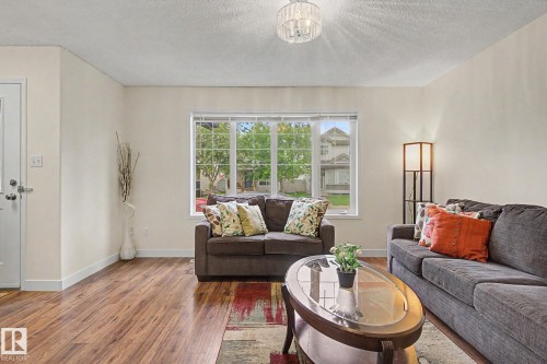 Bright living area featuring wood-finish flooring, a large multi-pane window, white trim, and a frosted glass chandelier - 710 Glenwright Court, Edmonton, AB 