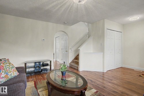 Open-concept living area featuring wood-finish flooring, a carpeted staircase, and an arched doorway - 710 Glenwright Court, Edmonton, AB 