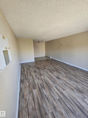 Spacious interior featuring wood-finish flooring, neutral-toned walls, and a textured ceiling - 301 10615 110 Street Nw, Edmonton, AB 