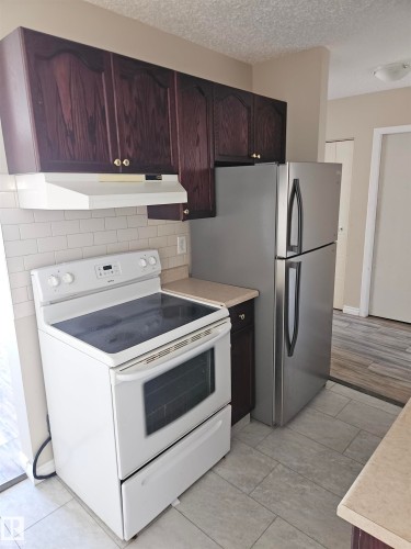 Kitchen with dark wood cabinetry, white subway tile backsplash, white electric range, stainless steel refrigerator, and light-toned countertops - 301 10615 110 Street Nw, Edmonton, AB 