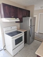 Kitchen with dark wood cabinetry, white subway tile backsplash, white electric range, stainless steel refrigerator, and light-toned countertops - 