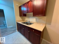 Kitchenette featuring dark wood cabinetry, a double basin stainless steel sink, beige laminate countertops, and a subway tile backsplash - 