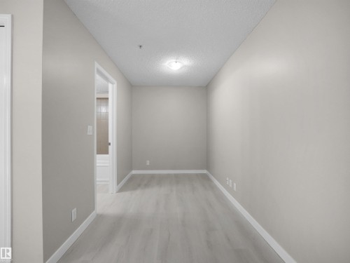 Neutral-toned hallway featuring light wood-finish flooring, white baseboards, and a flush-mount ceiling light - 220 12035 22 Avenue, Edmonton, AB 