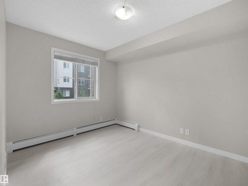 Bright room featuring light wood-finish flooring and a large window with white blinds - 220 12035 22 Avenue, Edmonton, AB 