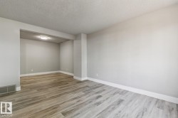 Spacious interior featuring light gray wall paint, wood-finish flooring, white baseboards, and a contemporary flush-mount ceiling light - 
