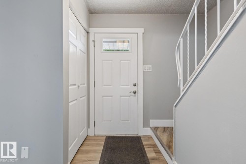 Entryway featuring light wood-finish flooring, a white paneled door with glass insert, and a white staircase with decorative balusters - 75 Mcleod Place, Edmonton, AB 