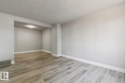 Spacious interior featuring light gray wall paint, wood-finish flooring, white baseboards, and a contemporary flush-mount ceiling light - 75 Mcleod Place, Edmonton, AB 
