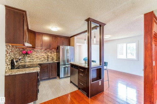 Kitchen featuring dark wood cabinetry, stainless steel appliances, a mosaic tile backsplash, and granite countertops - 16524 116 Street, Edmonton, AB 