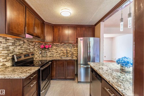Kitchen featuring rich wood cabinetry, granite countertops, stainless steel appliances, a mosaic tile backsplash, and ceramic tile flooring - 16524 116 Street, Edmonton, AB 