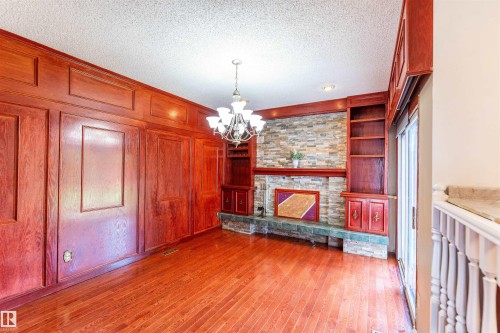 Warm wood-paneled room featuring rich wood-finish flooring, a stone-clad fireplace with a tile hearth, built-in shelving, and a prominent chandelier - 16524 116 Street, Edmonton, AB 