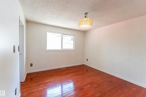 Room featuring wood-finish flooring, a contemporary drum pendant light fixture, white trim, and a window with white framing - 16524 116 Street, Edmonton, AB 