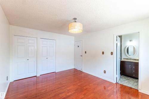Wood-finish flooring throughout, featuring a drum pendant light fixture, two bi-fold closets, and an entryway to a bathroom with a vanity and oval mirror - 16524 116 Street, Edmonton, AB 