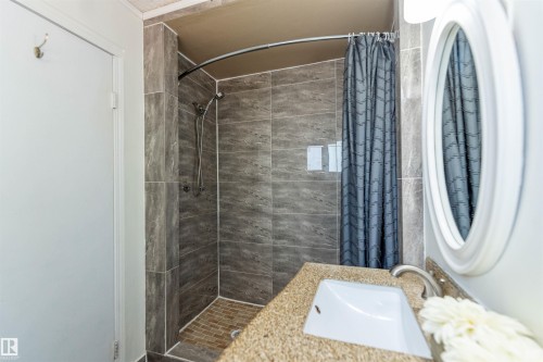 Bathroom featuring a tiled shower with a curved rod, a vanity with an integrated sink, a brushed nickel faucet, and an oval mirror - 16524 116 Street, Edmonton, AB 