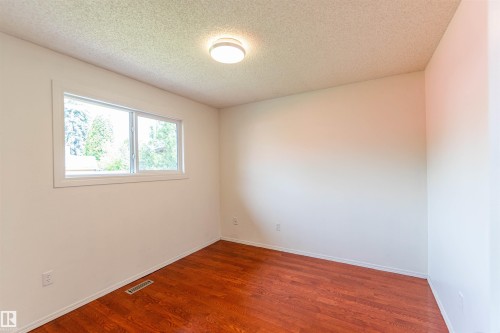 Room featuring wood-finish flooring, a white trim window, a ceiling-mounted light fixture, and light-colored walls - 16524 116 Street, Edmonton, AB 