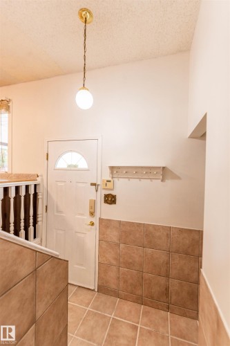 Entryway featuring a white paneled door with a half-moon window, globe pendant light fixture, and ceramic tile flooring - 16524 116 Street, Edmonton, AB 