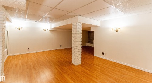 Spacious room featuring wood-finish flooring, white painted brick architectural accents, and a drop ceiling - 16524 116 Street, Edmonton, AB 