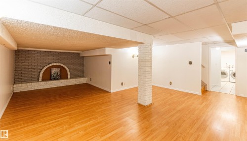 Spacious lower level featuring wood-finish flooring, a brick accent wall with a decorative arch, and a painted brick support pillar - 16524 116 Street, Edmonton, AB 