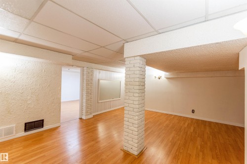 Spacious room featuring wood-finish flooring, a drop ceiling, and a painted brick column - 16524 116 Street, Edmonton, AB 