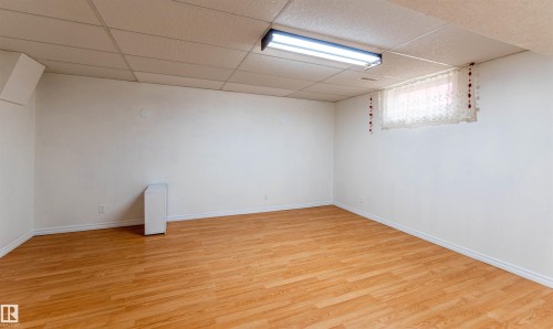 Spacious room featuring wood-finish flooring, white baseboards, and a drop ceiling with integrated fluorescent lighting - 16524 116 Street, Edmonton, AB 