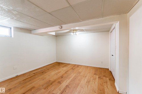 Spacious room featuring wood-finish flooring, white painted walls, and a drop ceiling - 16524 116 Street, Edmonton, AB 