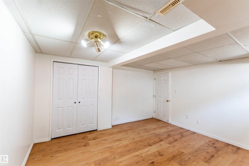 Room featuring wood-finish flooring, white painted walls, a drop ceiling with recessed lighting, and a bi-fold closet door - 16524 116 Street, Edmonton, AB 