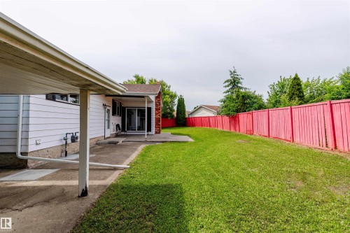 Expansive grassy backyard featuring a vibrant privacy fence, concrete patio, and a covered carport with direct access to the home - 16524 116 Street, Edmonton, AB 