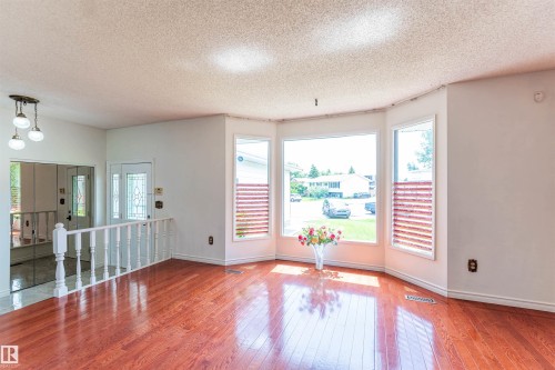 Bay window with three panes, featuring wood-finish flooring and a white spindle railing - 16524 116 Street, Edmonton, AB 