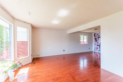 Spacious interior featuring warm wood-finish flooring, white walls, and a large bay window - 16524 116 Street, Edmonton, AB 