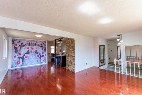 Open concept living area featuring rich hardwood flooring, a decorative accent wall, and a staircase with a classic white railing - 16524 116 Street, Edmonton, AB 