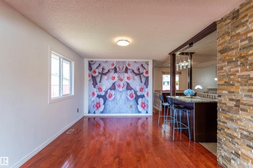 Hardwood-finish flooring extending from the foreground, leading to a breakfast bar with a stone countertop and built-in cabinetry - 16524 116 Street, Edmonton, AB 