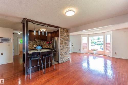Kitchen island with breakfast bar and granite-style countertop, featuring dark wood cabinetry and a mosaic tile backsplash - 16524 116 Street, Edmonton, AB 