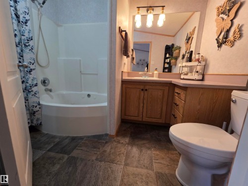 Bathroom featuring a jetted tub-shower combination, wood-finish vanity with countertop, and a vanity mirror with overhead lighting - 88B 3400 48 Street, Stony Plain, AB 