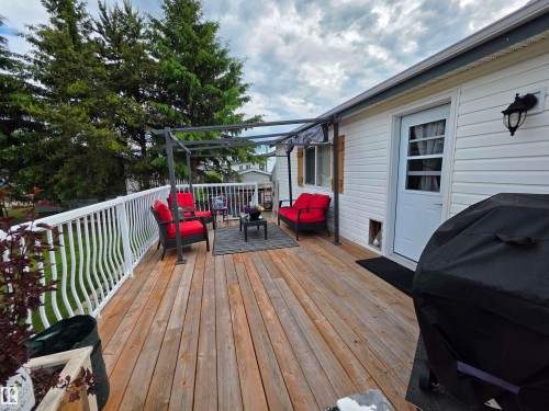 Spacious wood-plank deck featuring white railing with decorative balusters, a metal pergola structure, and direct access to the home's white-paneled exterior via a white exterior door with window panels - 88B 3400 48 Street, Stony Plain, AB 