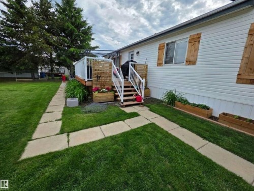 Backyard featuring a white exterior, a wood-finish deck with white railings, and a concrete paver pathway - 88B 3400 48 Street, Stony Plain, AB 