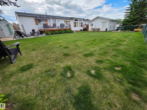 Expansive rear yard featuring a wooden deck, a concrete patio, a detached storage shed, white siding, and a chain-link fence - 88B 3400 48 Street, Stony Plain, AB 