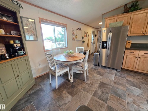 Kitchen and dining area featuring stone-look flooring, natural wood-finish cabinetry, a side-by-side stainless steel refrigerator, and a built-in hutch - 88B 3400 48 Street, Stony Plain, AB 