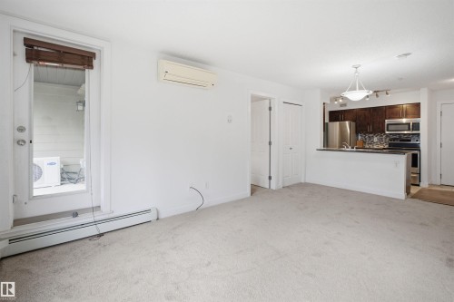 Open-concept living area featuring light-colored carpeting, a wall-mounted mini-split HVAC unit, and baseboard heating - 115 274 Mcconachie Drive, Edmonton, AB 