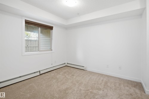 Carpeted interior space featuring a window with a brown roller blind, white baseboards, and white walls - 115 274 Mcconachie Drive, Edmonton, AB 
