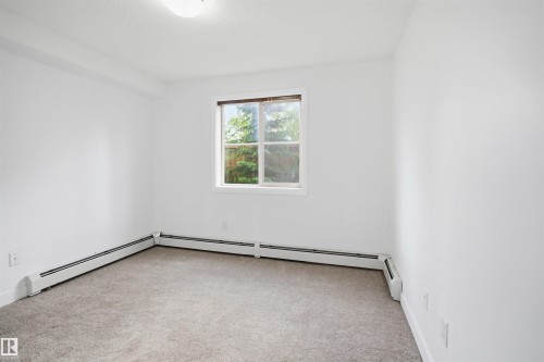 Bright room featuring a window with exterior tree scenery, light-colored carpeting, white baseboard heating units, and a ceiling-mounted light fixture - 115 274 Mcconachie Drive, Edmonton, AB 