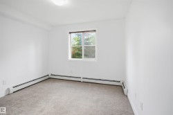 Bright room featuring a window with exterior tree scenery, light-colored carpeting, white baseboard heating units, and a ceiling-mounted light fixture - 