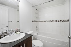 Bathroom featuring a white bathtub, white tiled shower surround with mosaic accent band, dark wood-finish vanity with an oval sink, and a large wall-mounted mirror - 