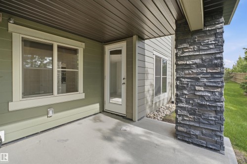 Covered concrete patio featuring a stone veneer pillar, green horizontal siding, and a glass-paneled exterior door - 115 274 Mcconachie Drive, Edmonton, AB 