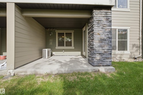 Covered patio featuring a stacked stone column, concrete pad, light siding, and an exterior door - 115 274 Mcconachie Drive, Edmonton, AB 