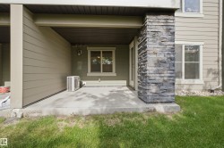Covered patio featuring a stacked stone column, concrete pad, light siding, and an exterior door - 