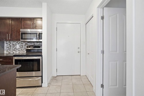 Kitchen area featuring dark wood-finish cabinetry, stainless steel appliances, and a mosaic tile backsplash - 115 274 Mcconachie Drive, Edmonton, AB 